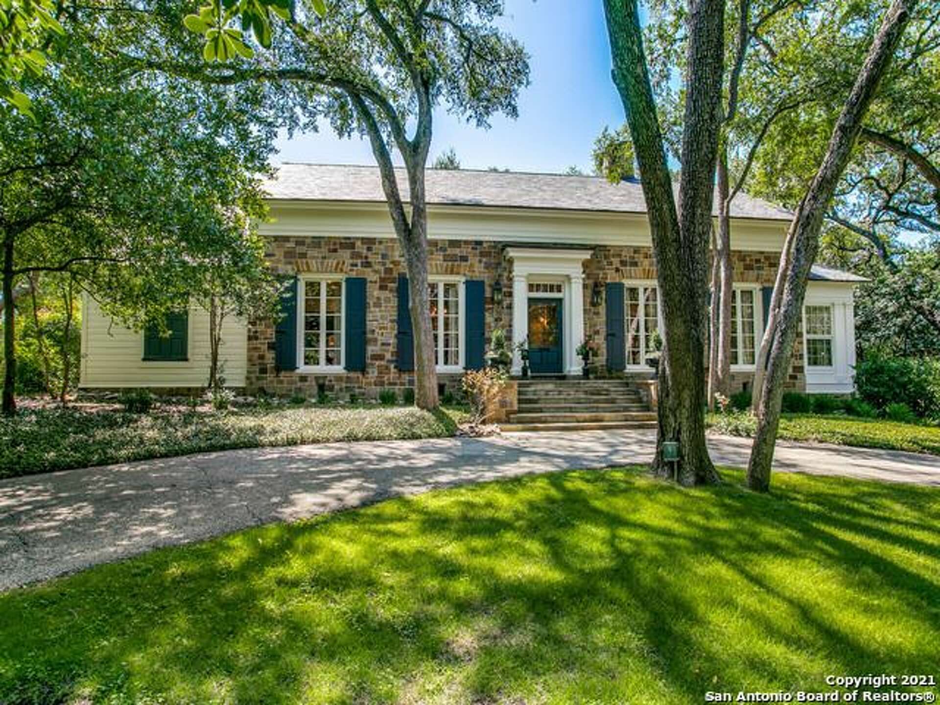 Historic stone residence with blue shutters and a tree-lined circular drive