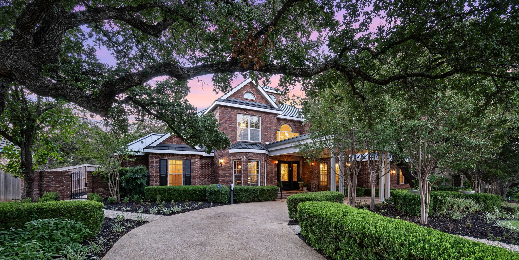 Traditional brick estate beneath mature oak trees at dusk